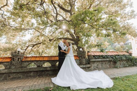 Foto für Braut und Bräutigam stehen und umarmen sich in einem schönen Hof. Weitwinkelbild des Sonnenuntergangs. - Lizenzfreies Bild