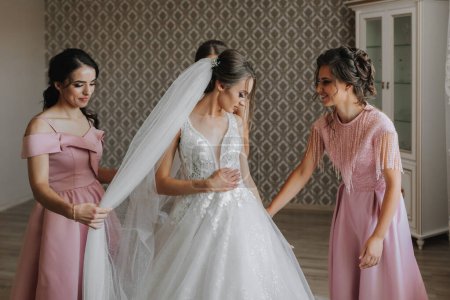 die Braut, mit ihren Freundinnen in passenden rosa Kleidern, hilft der Braut am Morgen, sich auf die Hochzeitszeremonie vorzubereiten