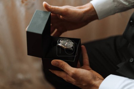 Photo for Close-up of a cropped shot of a man in an expensive classic suit looking at a watch. A man unwraps a gift. A handsome man with a precious watch in his hands. - Royalty Free Image