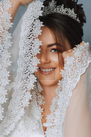 Téléchargez les photos : La timide mariée se couvre des manches de sa robe de dentelle. Portrait d'une mariée brune avec une tiare sur la tête et maquillage professionnel - en image libre de droit
