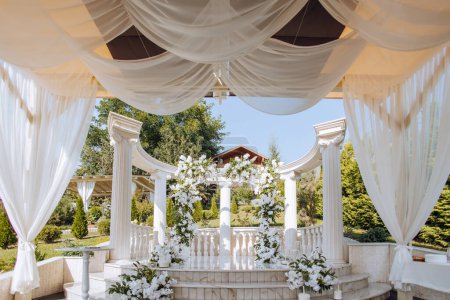 Foto de La ceremonia de la boda está decorada con flores frescas en el lugar con altas columnas blancas. Preparación para la ceremonia de boda - Imagen libre de derechos