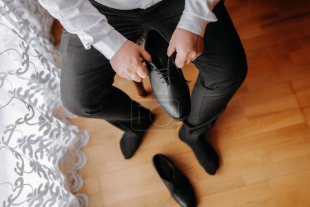 Téléchargez les photos : Un homme élégant porte des chaussures formelles en cuir noir. Des chaussures attachantes. Homme d'affaires attachant des lacets sur le sol. Le marié se prépare pour le mariage.. - en image libre de droit