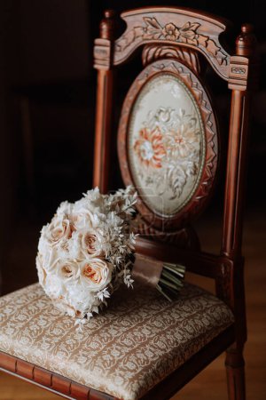 Téléchargez les photos : Style maison. Bouquet de mariage de fleurs crème et rose sur une chaise à la maison sous la lumière du jour. Détails de la mariée et du marié. - en image libre de droit