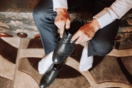 Téléchargez les photos : Un homme élégant porte des chaussures formelles en cuir noir. Des chaussures attachantes. Homme d'affaires attachant des lacets sur le sol. Le marié se prépare pour le mariage.. - en image libre de droit