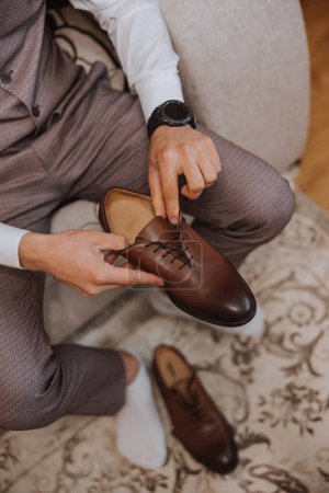 Téléchargez les photos : Un homme élégant porte des chaussures formelles en cuir marron. Des chaussures attachantes. Homme d'affaires attachant des lacets sur le sol. Le marié se prépare pour le mariage.. - en image libre de droit