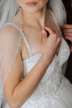 Téléchargez les photos : La mariée touche le pendentif sur son cou avec ses doigts. Préparation du mariage. Fête de mariage. - en image libre de droit