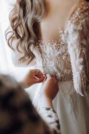 Photo for A woman is getting ready for a wedding and is adjusting her dress. The dress is white and has a lot of sparkles on it. The woman is wearing a necklace and a ring. The scene is intimate and romantic - Royalty Free Image