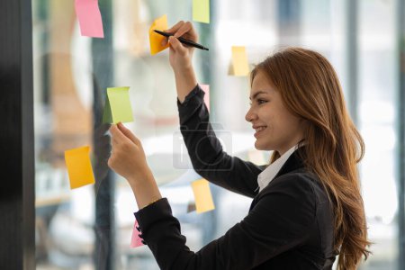Téléchargez les photos : Happy businesswoman planning ideas project work on a glass of wall with colorful memo - en image libre de droit