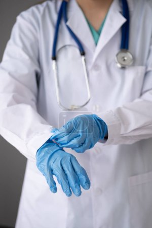 Foto de Enfermera doctora con máscara que se pone guantes médicos, doctora con uniforme blanco que usa máscara y guantes de goma - Imagen libre de derechos