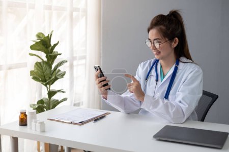 Photo for Female Young Asian doctor making video call with patient by smartphone cell phone laptop tablet - Royalty Free Image
