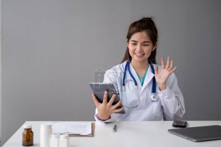 Téléchargez les photos : Femme Jeune médecin asiatique faire appel vidéo avec le patient par téléphone portable smartphone tablette ordinateur portable - en image libre de droit