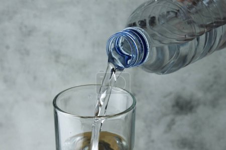 Foto de Verter agua de la botella en vidrio sobre fondo gris y textura - Imagen libre de derechos