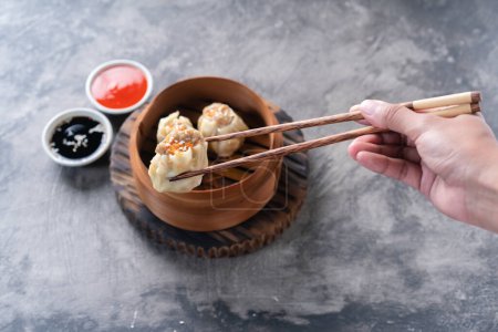 Photo for Chinese steamed dumplings or  Dim Sum with chopstick in bamboo steamer on dark abstract background - Royalty Free Image