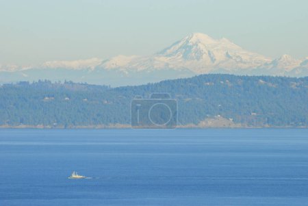 Photo for A tugboat traverses and ocean pathway with the San Juan Islands and the beautiful Mount Baker in behind - Royalty Free Image