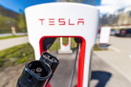 Photo for Tesla Superchargers on a parking lot, with a hand holding the CCS Type 2 plug. - Royalty Free Image