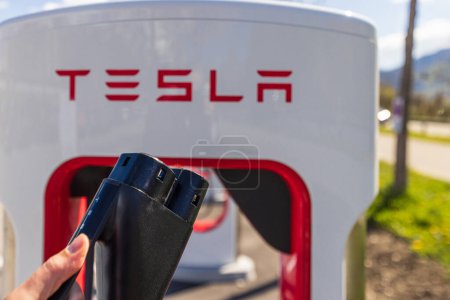 Photo for Tesla Superchargers on a parking lot, with a hand holding the CCS Type 2 plug. - Royalty Free Image
