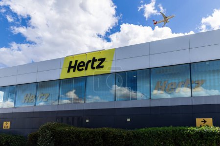 Photo for Hertz Car Rental at London Heathrow Airport with a plane flying over the building. - Royalty Free Image