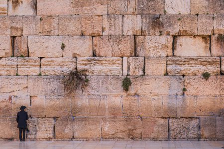 Vista trasera de un judío no revelado que llevaba sombrero y yarmulke mientras se enfrentaba al Muro de los Lamentos