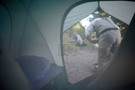 Photo for View through the open flap of a tent of two men working in a campsite in early morning mist or smoke from a camp fire - Royalty Free Image