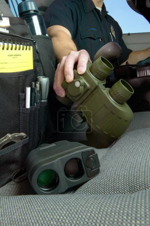 Photo for Police officer reaching for binoculars on the front seat of his vehicle in a low angle view of his hand - Royalty Free Image