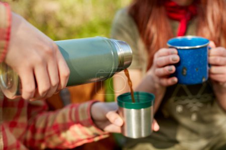 Photo for Two women sharing a thermal flask of coffee outdoors in nature as they take a rest from a day of hiking - Royalty Free Image