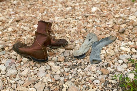 Téléchargez les photos : Paire de vieilles bottes en cuir marron lacées et chaussettes sales couchées sur un sol pierreux vu sous un angle élevé - en image libre de droit
