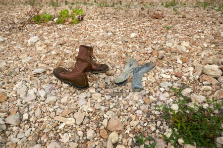 Téléchargez les photos : Paire de vieilles bottes en cuir marron et chaussettes sales couchées côte à côte sur un sol pierreux avec espace de copie - en image libre de droit