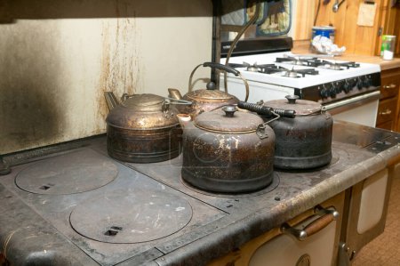 Photo for Four old blackened metal kettles on a rustic wood burning stove in an annexe to a house or hut kitchen probably used for camping over a fire - Royalty Free Image