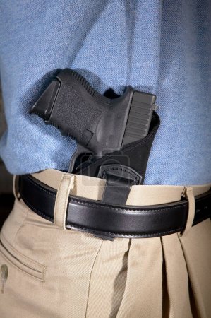 Man wearing a handgun in a clip on webbing holster tucked into the waistband of his pants in a close up side view