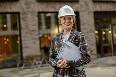 Photo for Woman architect in white helmet holding tablet and looking at camera on city building background - Royalty Free Image
