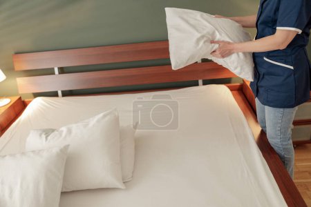 Photo for Woman is putting fresh pillow on bed during cleaning process in a hotel room - Royalty Free Image