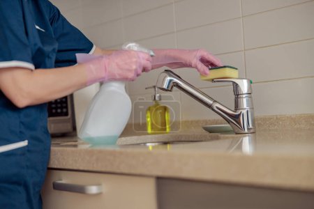 Foto de Manos de mujer en guantes protectores limpiando grifo con esponja y spray. Concepto general de limpieza - Imagen libre de derechos