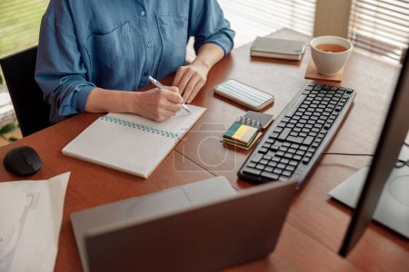 Photo for Woman taking notes while working in cozy home office remotely. High quality photo - Royalty Free Image