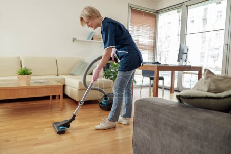 Photo for Professional Cleaning lady wearing uniform vacuums floor in living room. High quality photo - Royalty Free Image