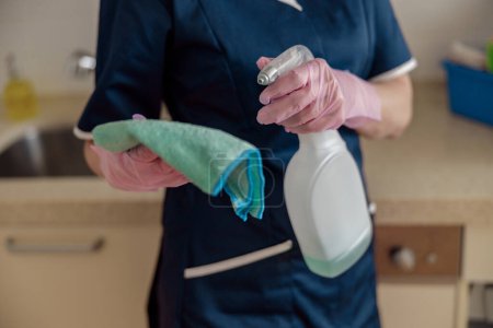 Téléchargez les photos : Femme de nettoyage dans le masque nettoie table de travail utiliser chiffon et des produits de détergent efficaces dans la cuisine - en image libre de droit