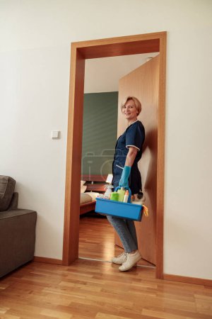 Téléchargez les photos : Femme de nettoyage professionnelle tient boîte avec des détergents et des chiffons et caméra de regard. Photo de haute qualité - en image libre de droit