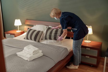Foto de Mujer está poniendo almohada en la cama durante el proceso de limpieza en una habitación de hotel - Imagen libre de derechos