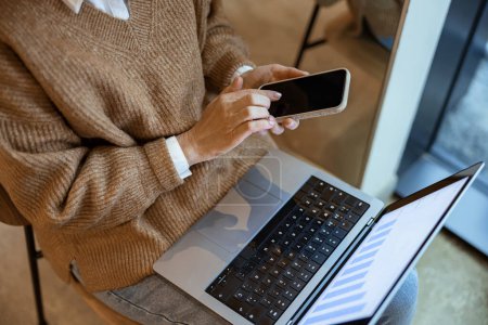 Téléchargez les photos : Femme méconnaissable travaille à distance et en utilisant un ordinateur portable et un téléphone tout en étant assis dans le coworking - en image libre de droit