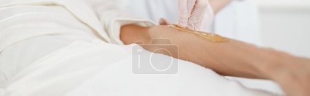 Foto de Mujer que se somete a un procedimiento de depilación en el brazo con pasta de azúcar en el salón de belleza, de cerca, encerado - Imagen libre de derechos