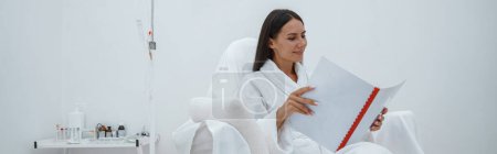 Photo for Woman in white bathrobe reading magazine while sitting in luxury wellness spa centre - Royalty Free Image