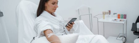Photo for Woman in white bathrobe use phone during medical procedure in beauty clinic. High quality photo - Royalty Free Image