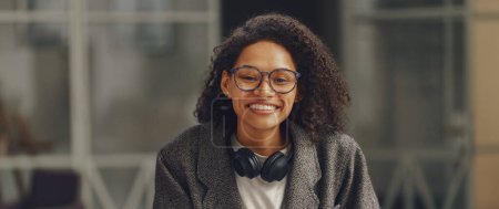 Téléchargez les photos : Femme freelance souriant à la caméra tout en étant assis avec le téléphone dans le coworking moderne. Photo de haute qualité - en image libre de droit