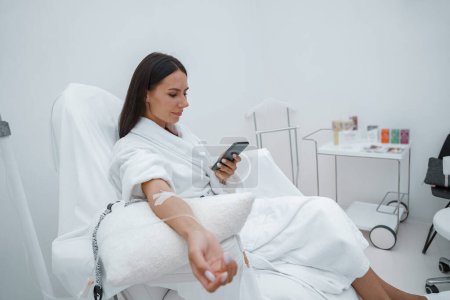 Foto de Mujer en albornoz blanco usar el teléfono durante el procedimiento médico en la clínica de belleza. Foto de alta calidad - Imagen libre de derechos