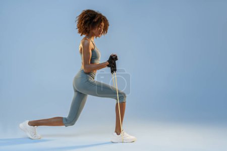 Photo for Side view of woman performs exercises with expander on studio background. Strength and motivation - Royalty Free Image
