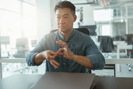 Foto de Empresario asiático usando lenguaje de señas con colegas mientras está sentado en el cargo. Foto de alta calidad - Imagen libre de derechos