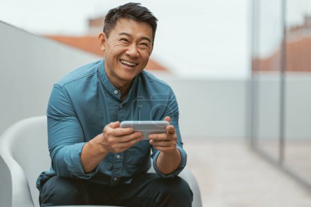 Foto de Sonriente asiático hombre de negocios utilizando el teléfono durante el descanso. Foto de alta calidad - Imagen libre de derechos