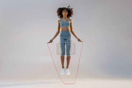 Téléchargez les photos : Femme sportive en vêtements de sport sauter avec corde à sauter sur fond de studio. Meilleur entraînement cardio - en image libre de droit