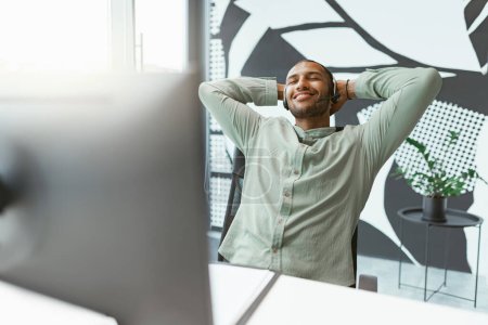 Téléchargez les photos : Heureux homme d'affaires africain se reposer après avoir travaillé sur ordinateur au bureau. Photo de haute qualité - en image libre de droit