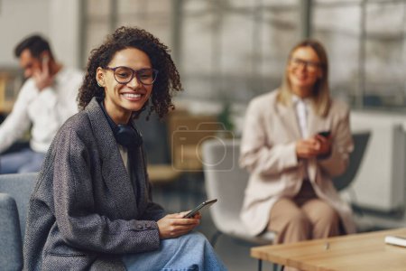 Téléchargez les photos : Femme freelance assis avec téléphone en coworking sur fond de collègues. Photo de haute qualité - en image libre de droit