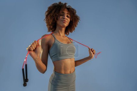 Foto de Mujer deportiva en ropa deportiva sosteniendo la cuerda de salto en el fondo del estudio. El mejor entrenamiento cardiovascular - Imagen libre de derechos